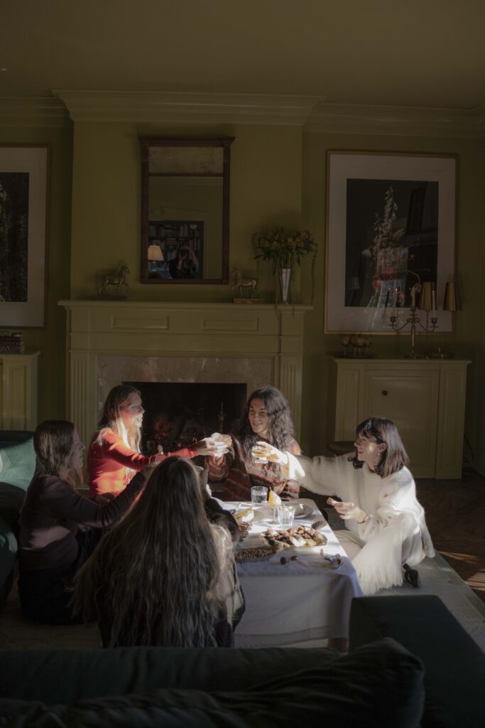 Five friends sit around a coffee table and cheers with glasses of bubbly at an afternoon dessert party