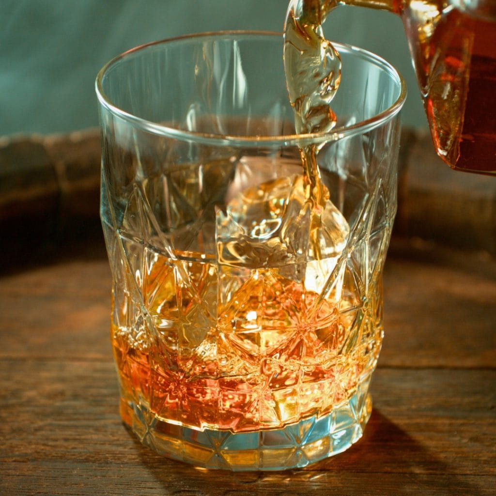 Rum being poured into a glass for a dark and stormy cocktail. The glass is cut crystal and it is placed on a wooden tray.