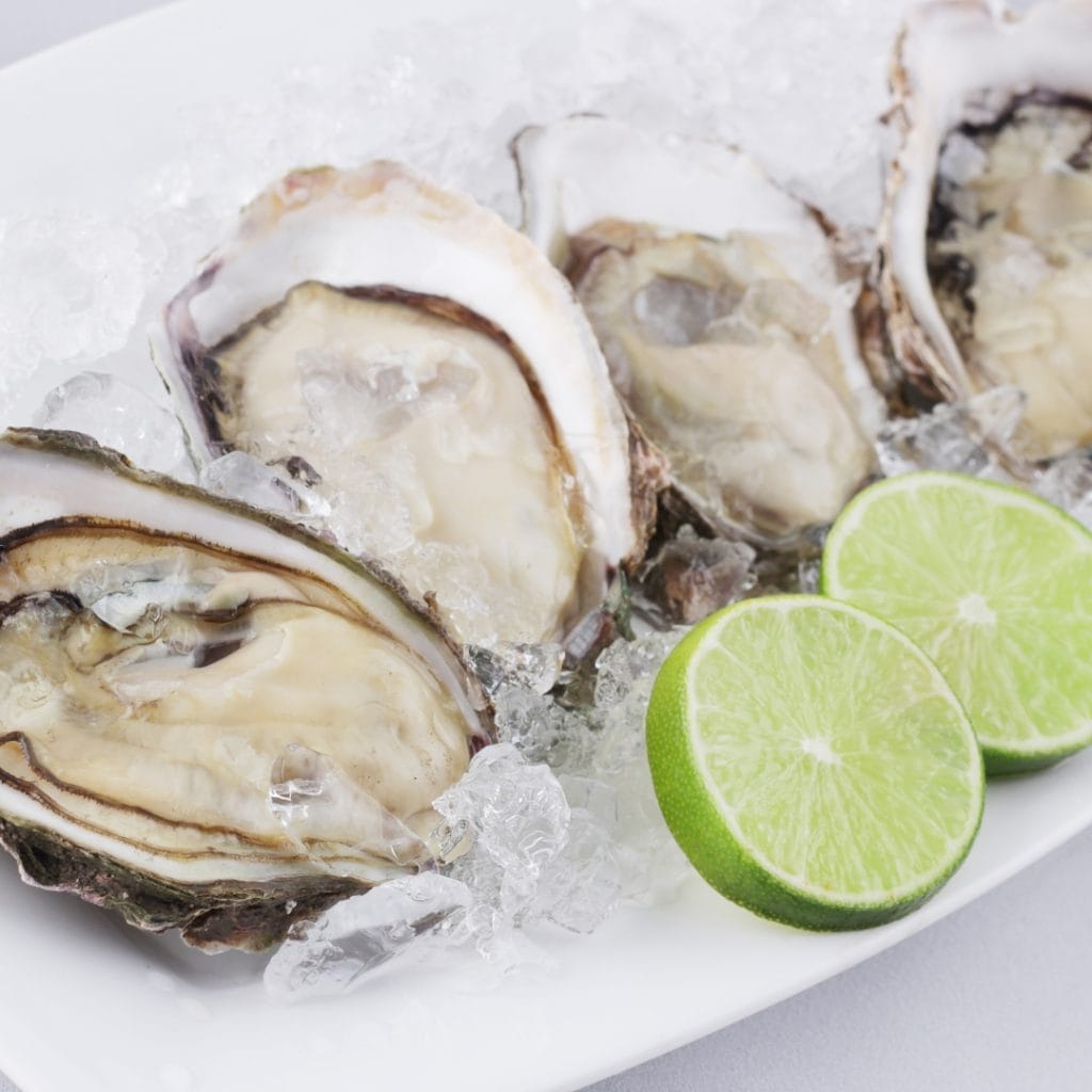 Image of a white platter with oysters on ice and two sliced limes being served at a Perfect Couple cocktail party.