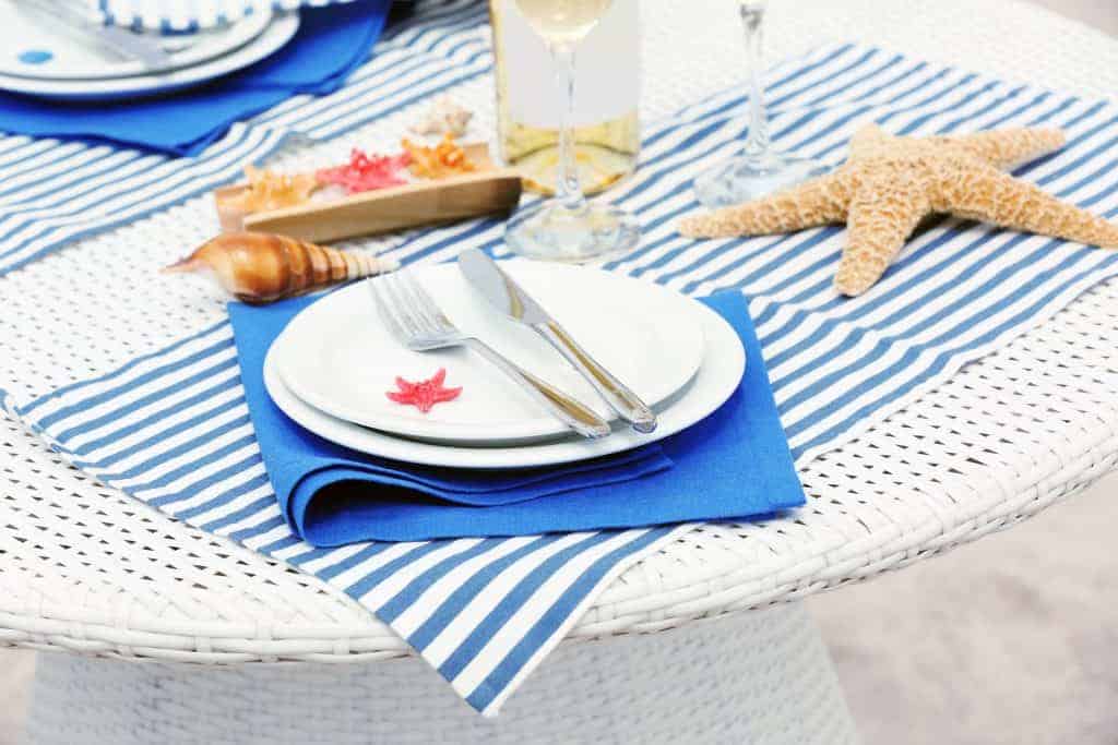 Set table decorated in marine style with blue and white striped place mats and runners, simple blue napkins and simple ocean decor for an ocean-themed party.