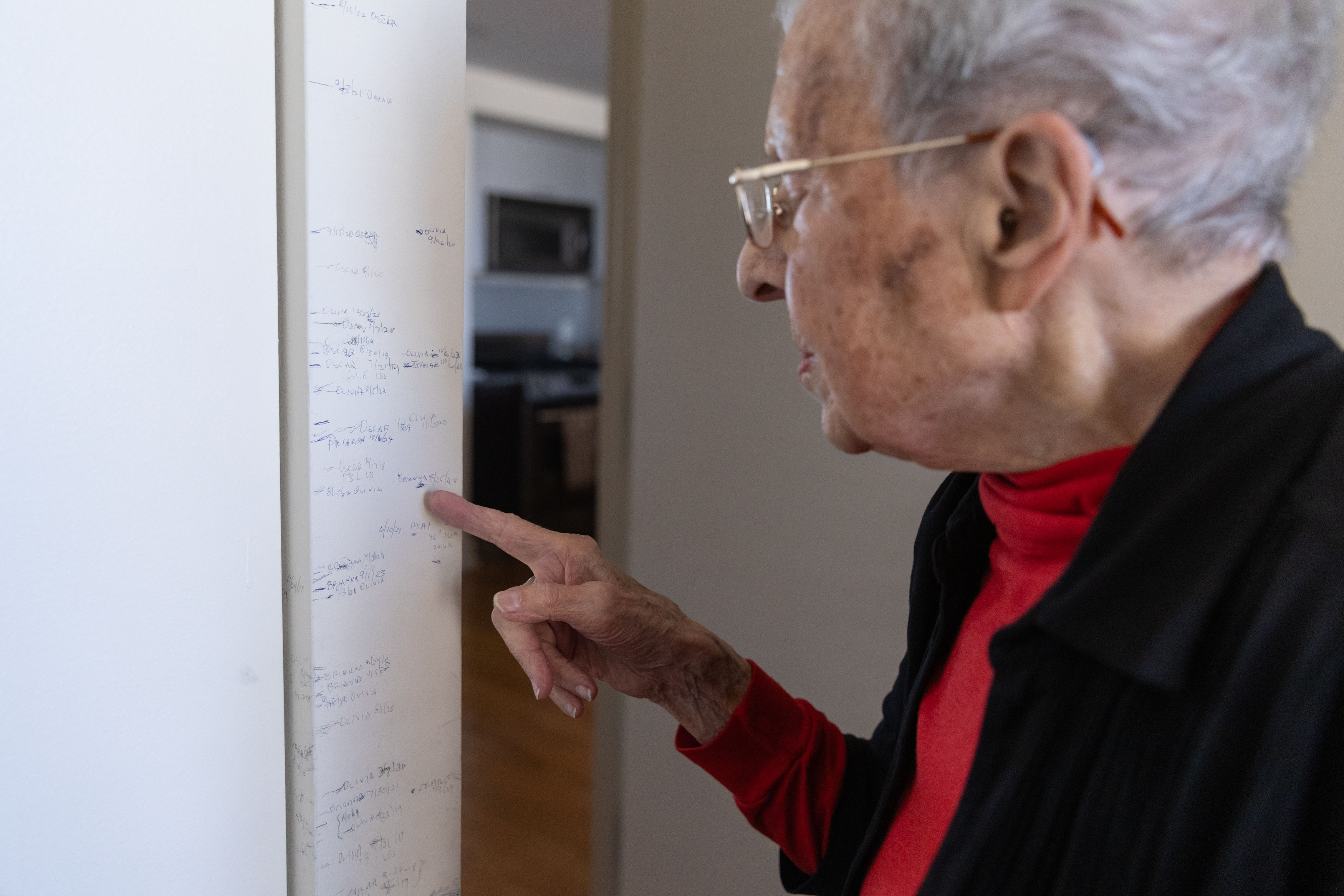 A photo of a senior woman pointing to pencil marks on a doorway.