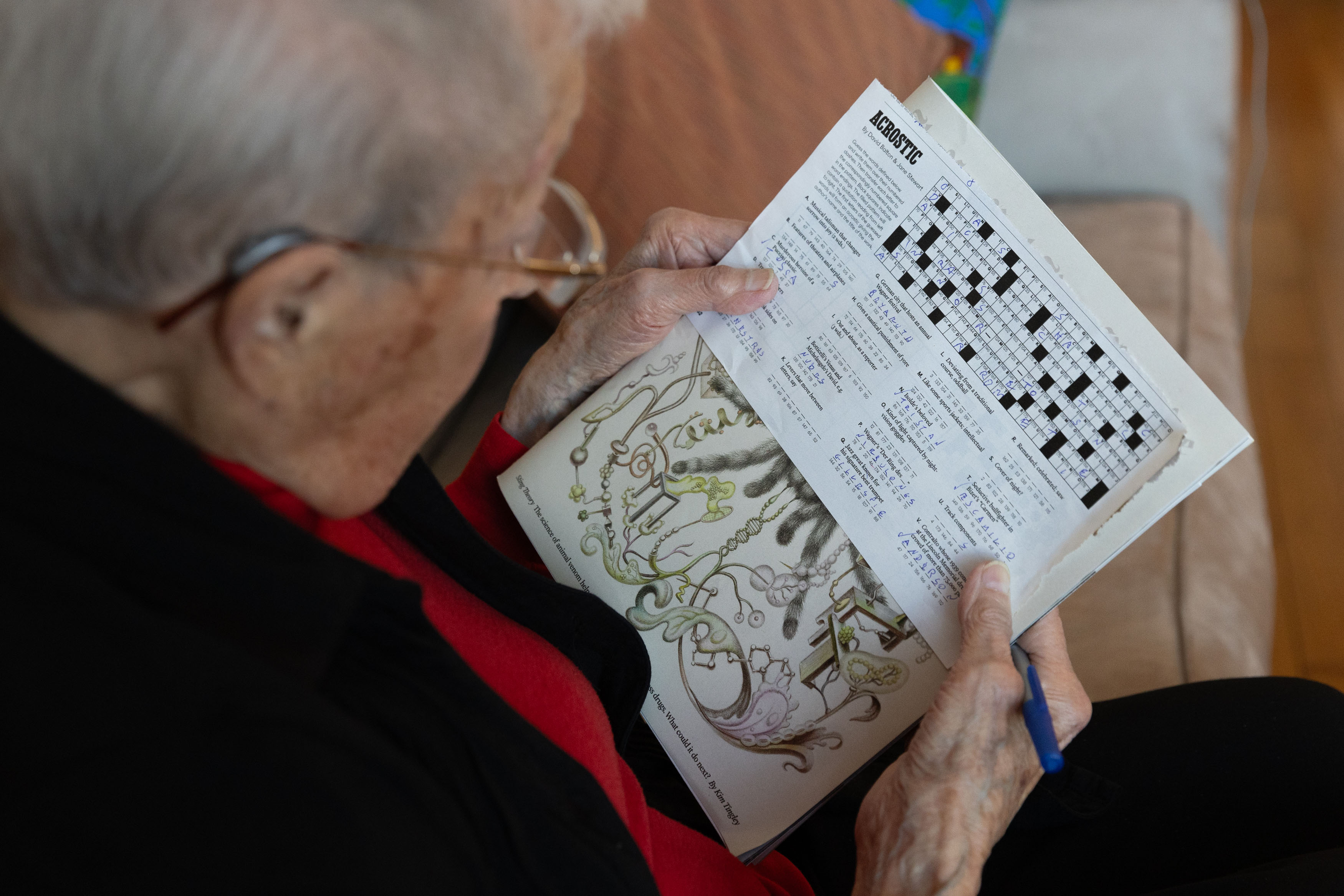 A photo taken over the shoulder of a senior woman writing the crossword puzzle.