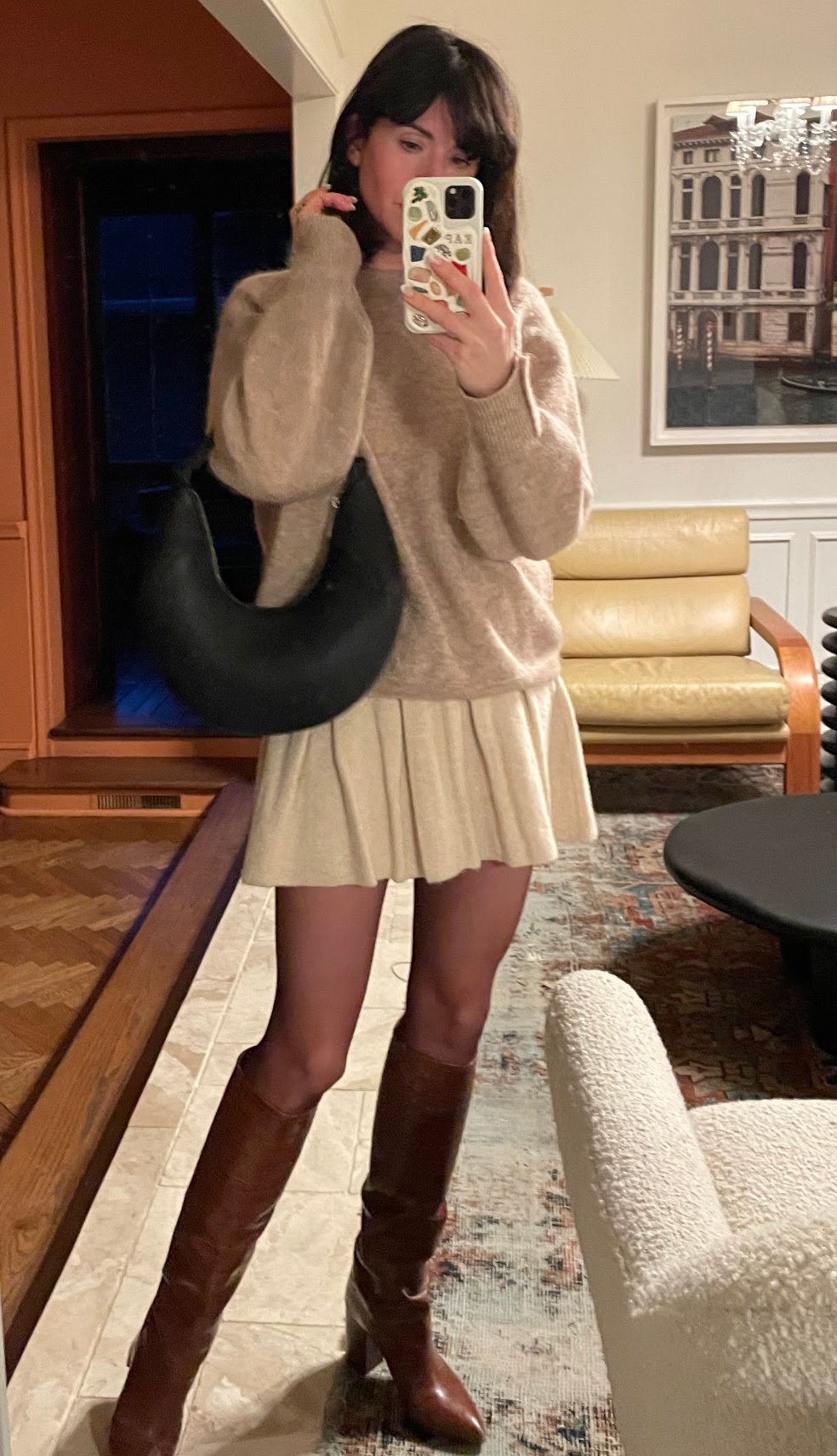 A woman wears a beige sweater, cream mini skirt, brown sheer tights, heeled tall brown boots, and a black handbag