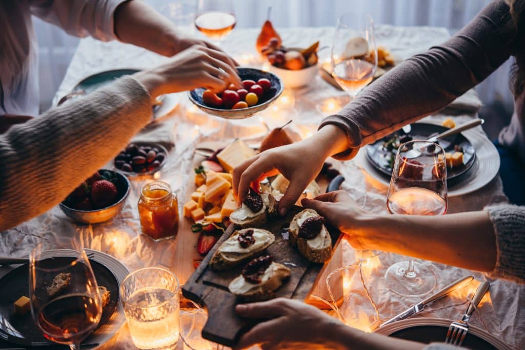 Friends having a dinner party with different kinds of appetizers and rose wine. The table is dimly lit with ambient lighting and guests are reaching for appetizers.