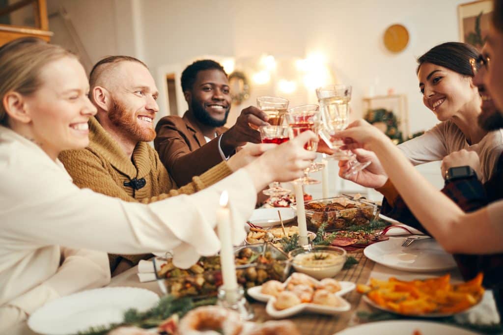 Multi-ethnic group of people raising glasses sitting at beautiful dinner table together sharing a meal.