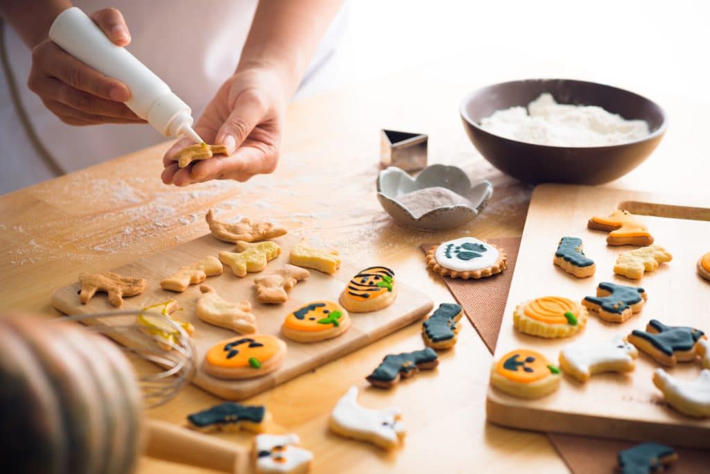 Close-up of baker decorating Halloween cookies with frosting. There are pumpkins, bats, and ghosts.