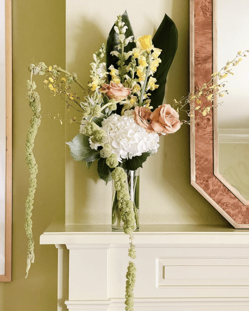 A vase of beautifully arranged flowers sits on green living room mantel