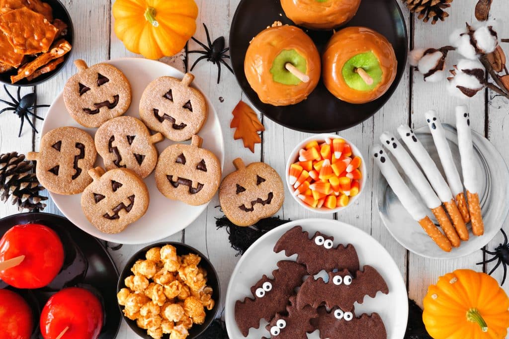 Rustic Halloween treat table scene over a white wood background. Overhead view. Selection of candied apples, cookies, candy and sweets.