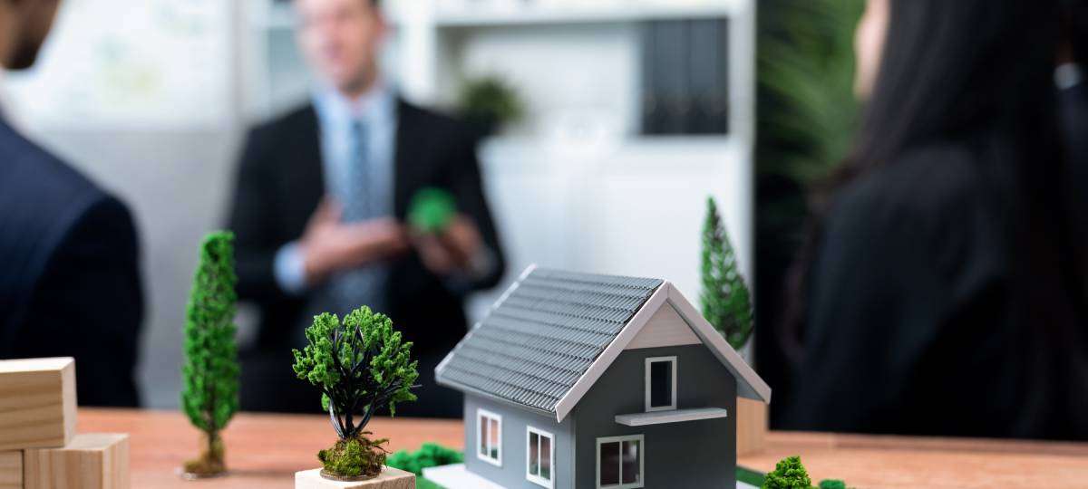 A model building showcasing eco-friendly design and landscaping. In the background, business professionals discuss designs.