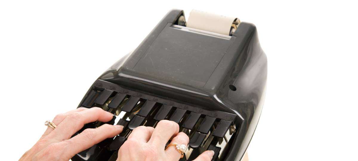 A woman's hands placed meticulously on the keys of a stenotype machine, waiting to begin taking notes.