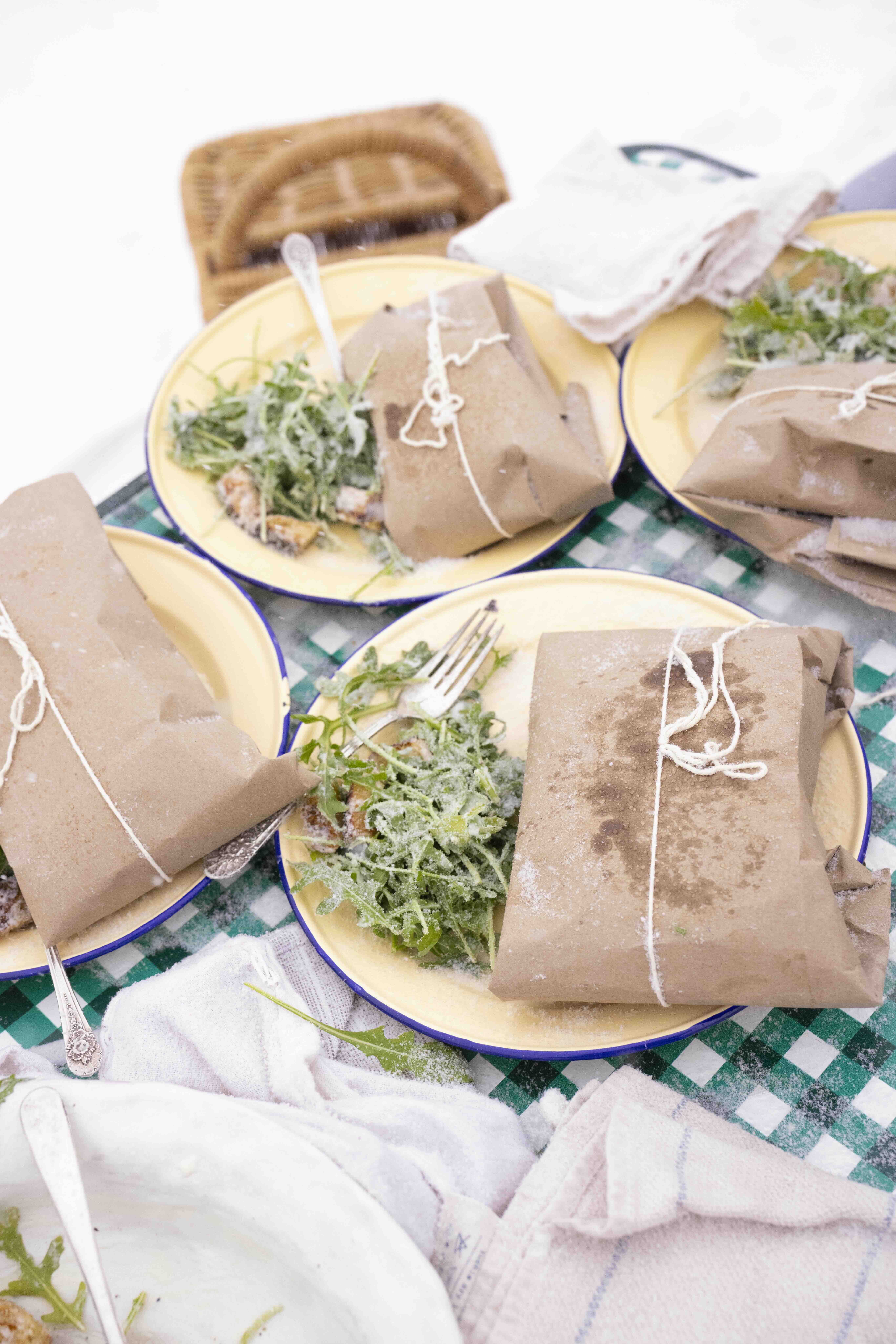 In a snowy outdoor landscape, a table is set with a green and white gingham tablecloth. Four yellow plates are topped with arugula salad and warm grilled cheddar cheese sandwiches