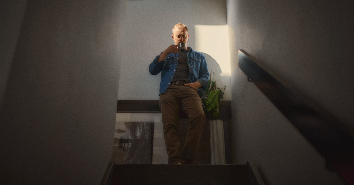 wide shot of mens casual outfit with medium blue denim western shirt over a black tshirt with brown jeans and tan converse sneakers