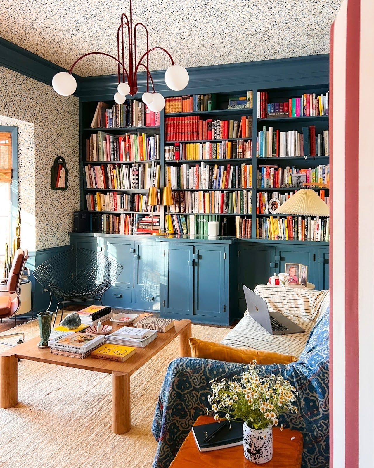 A cozy office features a built-in bookshelf painted blue, floral wallpaper, a wood coffee table, and a neutral rug from ECARPETGALLERY
